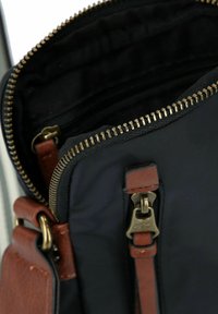 Schwarze Stofftasche mit einem Reißverschluss, braunen ledernen Akzenten und goldenen Beschlägen. Merkmale ein strukturiertes Innenleben und eine braune Riemenbefestigung.