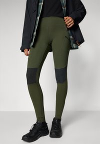 Olivgröna leggings med hög midja, svarta knälappar och sidofickor. Tillverkade av elastiskt tyg för komfort och rörelsefrihet.