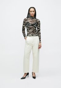 Κοντό, στενό τοπ μακρυμάνικο με μαύρες και μπεζ ρίγες ζέβρας, συνδυασμένο με ψηλόμεσα λευκά παντελόνια και μαύρα ψηλοτάκουνα στιλέτο.