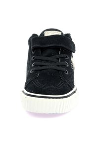 Las zapatillas de gamuza negra cuentan con una punta redondeada, un frente con cordones y una tira de velcro. Suela de goma blanca con una franja texturizada en la base.