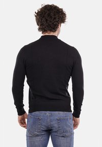 Maglione nero a maglia con colletto rotondo, design aderente e maniche lunghe, abbinato a jeans in denim blu chiaro con due tasche posteriori.