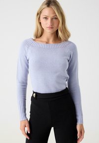 Suéter de manga larga color púrpura claro con escote barco, puños acanalados y textura suave, combinado con pantalones negros de cintura alta.