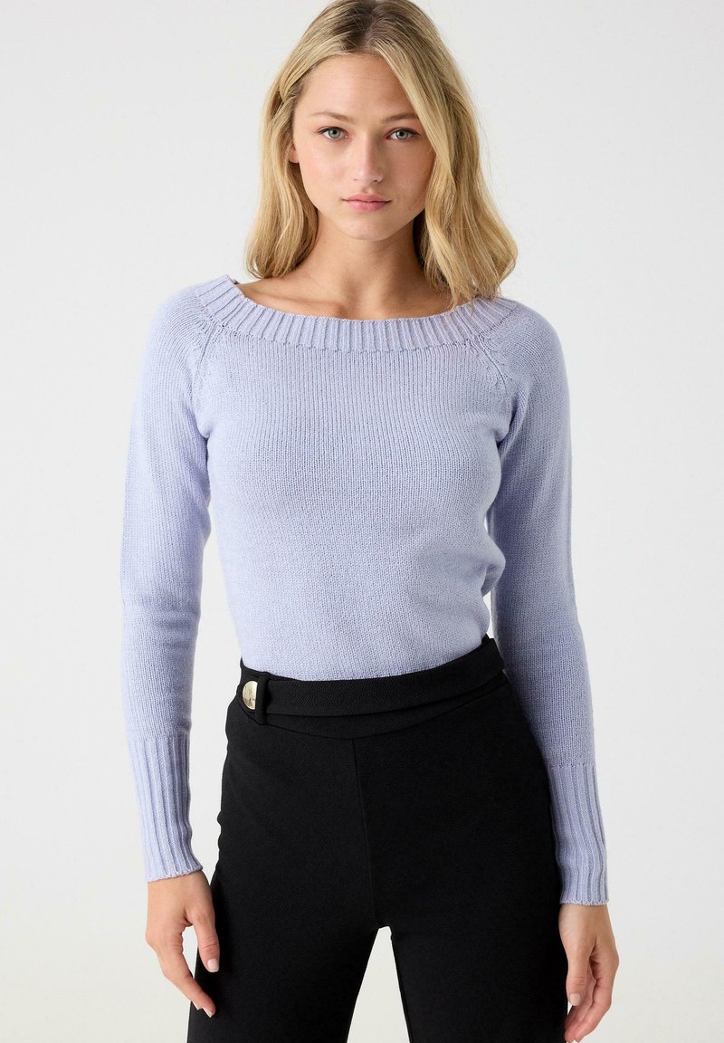 Suéter de manga larga color púrpura claro con escote barco, puños acanalados y textura suave, combinado con pantalones negros de cintura alta.