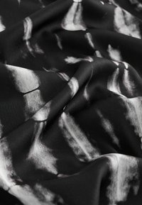 Sort stof med hvide abstrakte mønstre, har en glat tekstur og et subtilt skær, draperet i bløde folder.