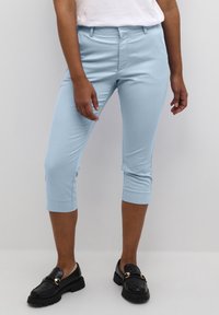 Light blue cropped pants made of a smooth fabric, featuring a fitted design and rolled cuffs. Paired with black loafers for contrast.