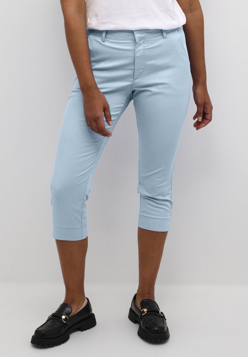 Light blue cropped pants made of a smooth fabric, featuring a fitted design and rolled cuffs. Paired with black loafers for contrast.