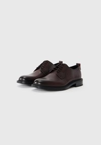 Chaussures en cuir brun à lacets avec une finition lisse, bout rond et semelle en caoutchouc noir. Comprend des coutures discrètes et une languette à l'arrière pour un enfilage facile.