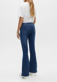Džíny s rozšířenými nohavicemi z tmavě modrého denimu s zadními kapsami, doplněné bílým krátkým tričkem. Hladká textura a strukturovaný střih.