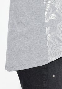 T-shirt grigio con un delicato motivo floreale sul lato. Realizzato in tessuto morbido con una vestibilità comoda, abbinato a jeans in denim scuro.