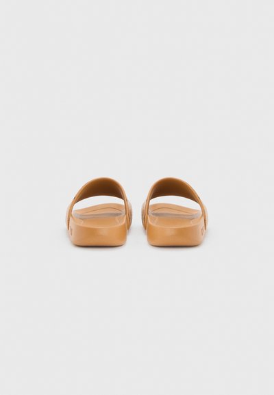 Paire de sandales slide de couleur sable avec larges brides et semelles moulées vues de dos sur un fond gris clair.