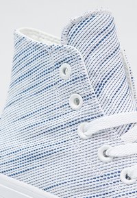 Modré a bílé vysoké tenisky se strukturou plátěného svršku se proužkovaným vzorem, bílými otvory na šněrování a plochými bílými šňůrkami.