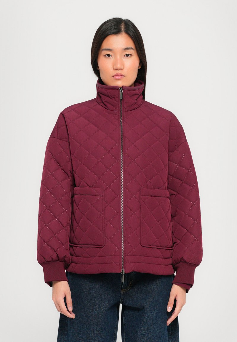 Burgundy quilted jacket with a high collar, front zip, and two large patch pockets; features ribbed cuffs and a textured finish.