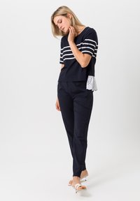 Marineblauw cropped top met witte horizontale strepen, voorzien van een kanten zoom. Gecombineerd met marineblauwe tapered broeken en witte haksandalen.