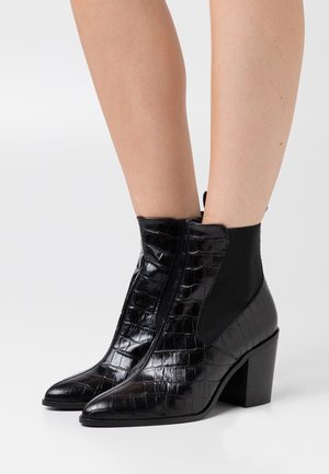 Svarta ankelboots i glansigt krokodiltexturerat läder. Har spetsig tå, elastiska sidopaneler och klumpiga klackar.