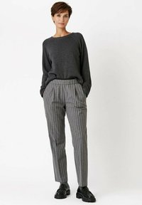 Grauer Pullover mit langen Ärmeln, kombiniert mit grauen gestreiften Hosen. Die Hosen haben einen elastischen Bund und seitliche Taschen; schwarze Schuhe.