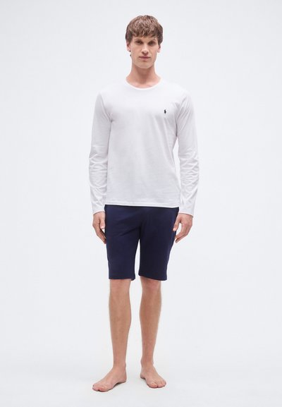 Langermet hvit bomullsskjorte med rund hals, kombinert med marineblå shorts, med avslappet passform og uten synlige mønstre.