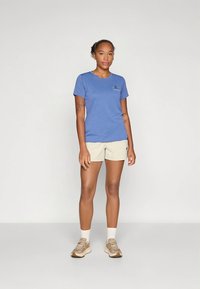 Blå kortärmad t-shirt med rund halsringning, kombinerad med beige shorts. Tyget ser mjukt ut och en liten logotyp syns på bröstet.