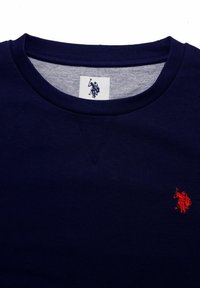 Marinblå sweatshirt i bomull med rund halsringning och korta ärmar. Anmärkningsvärd röd brodering av en ryttare-logotyp på bröstet.