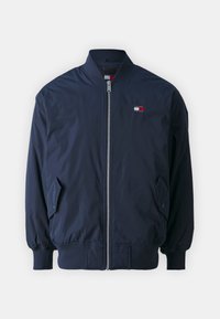 Námořnicky modrá bomber bunda se zipem, žebrovanými manžetami a pasem. Na hrudi má malý vyšívaný logo a boční kapsy. Hladká textura.