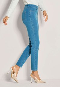 Blauwe denim skinny jeans met een middelhoge taille, met een soepele textuur en subtiele steekdetails. In combinatie met crèmekleurige hoge hakken.