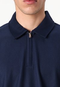 Marinblå zip-up polo-shirt med ribbad struktur och en formad krage. Dragkedjan är metallisk och ger en elegant finish.