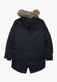 Parka de marina con capucha con borde de piel, mangas largas, puños negros y un detalle de lazo en la parte posterior, mostrada desde atrás sobre un fondo blanco.
