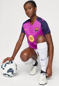 Nike FC Barcelona-drakt i lilla med marineblå ermer, med en Spotify-logo. Spilleren har på seg hvite sokker og fotballsko, og holder en fotball.