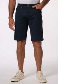 Námořnické modré bavlněné šortky s rovný střihem, opatřené zapínáním na knoflík, bočními kapsami a regular pasem. Nošeny s lehkými teniskami.