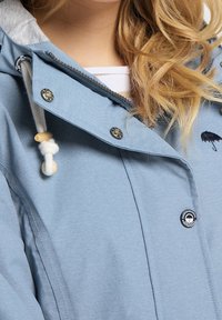 Ljusblå jacka med dragkedja framtill, huva med dragsko och silverfärgade detaljer. Har broderad paraplylogotyp och textil med struktur.