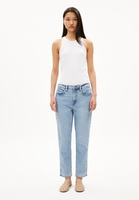 Débardeur blanc côtelé, jeans droit bleu clair avec cinq poches, et chaussures plates beiges. Design simple et décontracté.