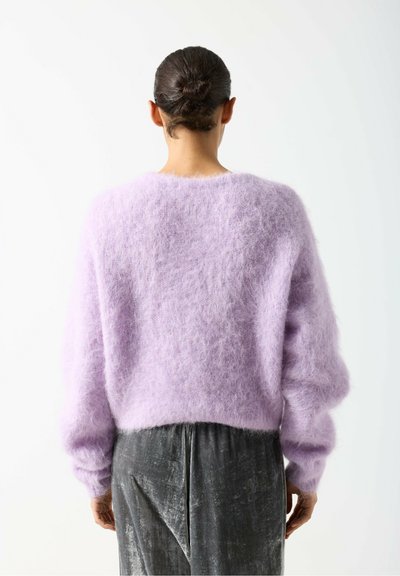 Pull en mohair lilas, coupe ample, manches larges, texture douce et duveteuse. Associé à un pantalon en velours gris.