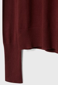 Pull bordeaux à texture côtelée, avec un ourlet et des poignets larges côtelés, mettant en valeur un matériau tricoté doux.