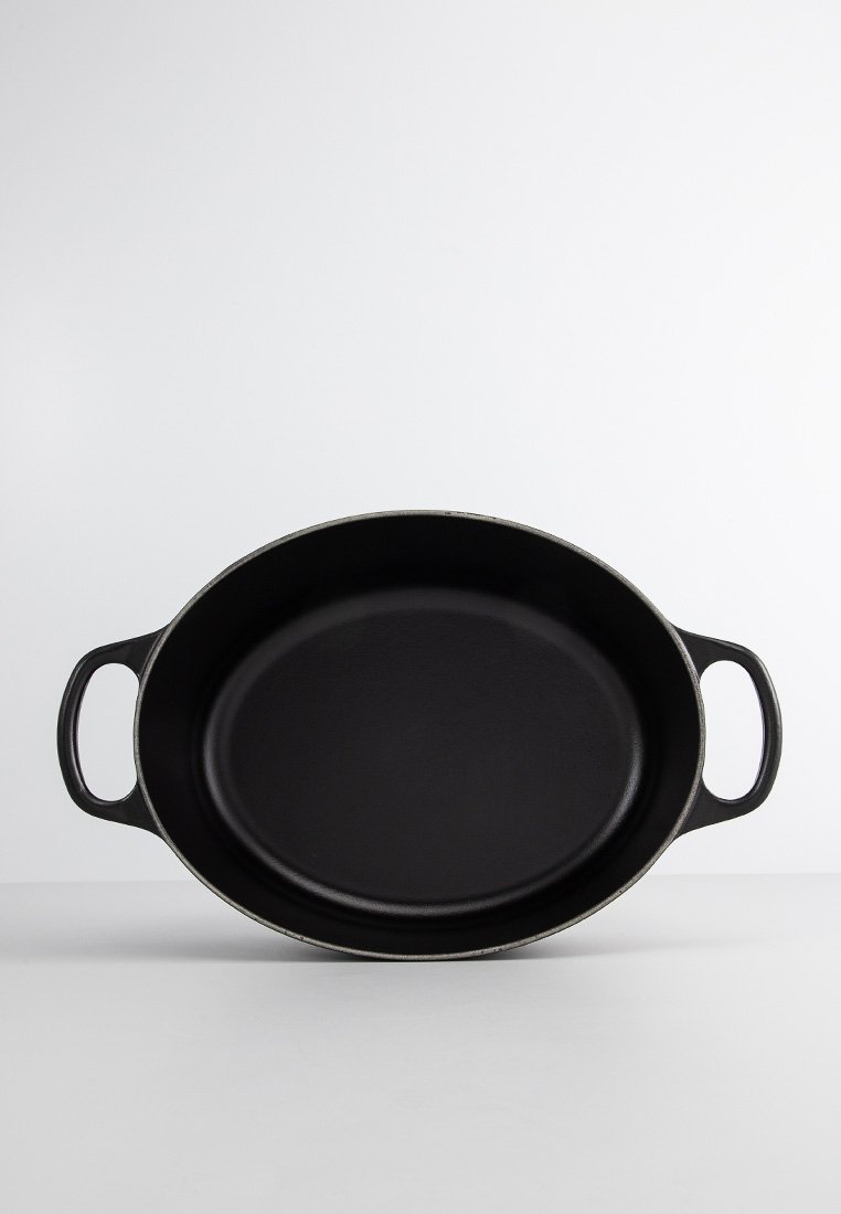 Schwarzer ovaler Gusseisen-Topf mit zwei seitlichen Griffen, glatter Innenfläche und strukturiertem Äußeren. Entworfen zum Kochen und Servieren.