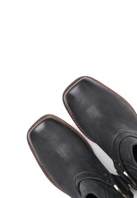 Melnas ādas potīšu zābaki ar kvadrātveida purngalu, ar brūnu dūrienu un sprādzi sānos. Gluda tekstūra, minimālisma dizains.