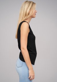 Zwarte mouwloze top met een gestructureerd patroon, aansluitend ontwerp en ronde zoom, gecombineerd met lichtblauwe jeans.