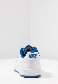 Fehér Nike sneaker kék szövetgallérral és kék logóval. A talpa textúrázott, az anyaga sima felületű, perforációkkal.