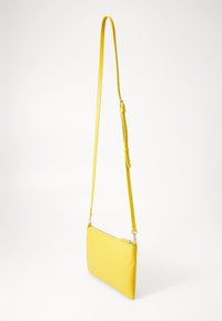 Sac bandoulière en cuir jaune avec une surface texturée, forme rectangulaire mince, bandoulière réglable et fermeture éclair en haut.