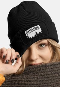 Black ribbed knit beanie with a logo patch featuring white text and a forest design. The texture appears soft and warm.