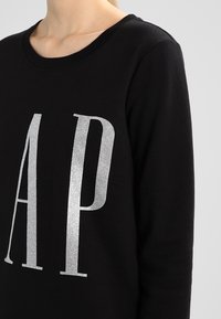 Felpa nera con collo rotondo, decorata con grandi lettere in glitter argento "A" e "P" sulla parte anteriore. Tessuto morbido con una texture liscia.