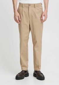 Beige tailored pants with a straight fit, belt loops, a button closure, and minimal creases. Worn with dark loafers. Smooth fabric texture.