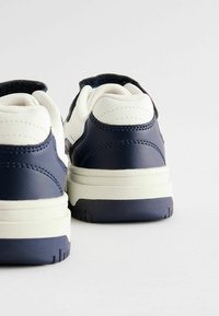 Navy and white sneakers with a textured leather finish, featuring a padded collar and a rubber sole with a patterned tread.