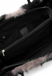 Black handbag with a soft grey fur trim, featuring a black interior with a zipper pocket and a textured leather logo patch inside.