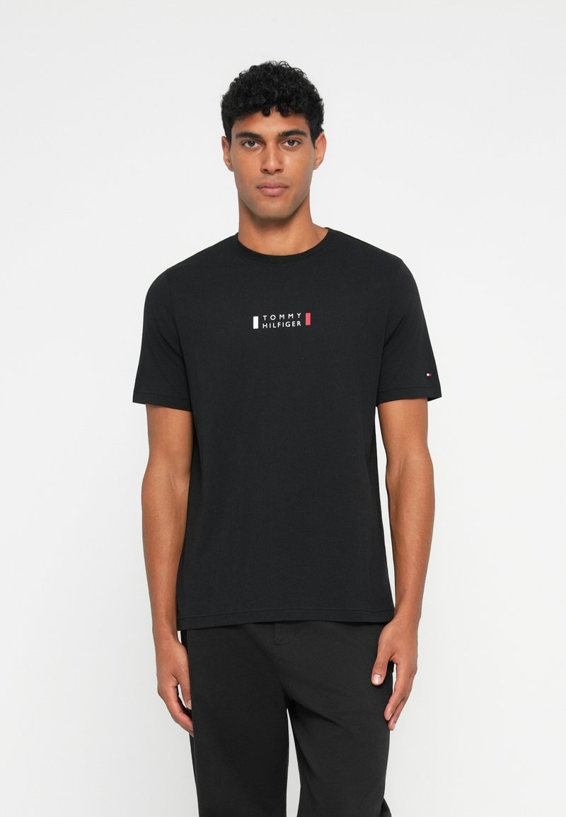 Μαύρο βαμβακερό T-shirt με στρογγυλή λαιμόκοψη, κοντά μανίκια και κεντρικό λογότυπο σε λευκό, κόκκινο και μπλε. Απλός, κλασικός σχεδιασμός.