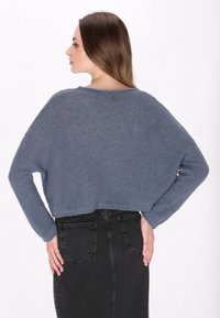 Pull bleu en maille, coupé avec un motif texturé, à manches longues et un large décolleté, associé à une jupe en denim noir ajustée.