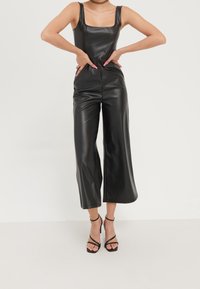 Svart jumpsuit i konstläder med fyrkantig halsringning, breda avkortade ben och sidofickor. Matchas med svarta klackar med tunna remmar.