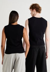 Black sleeveless tops, ribbed texture, worn with grey sweatpants and striped trousers, showcasing a casual, relaxed fit from the back.