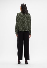 Πράσινο φλοράλ πουκάμισο με μακριά μανίκια, συγκεντρωμένα μπατζάκια και κολάρο πίσω. Συνδυάζεται με μαύρο παντελόνι σε ευρεία γραμμή και καφέ ψηλοτάκουνες γόβες.