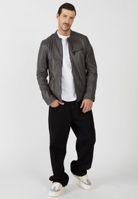 Szara skórzana kurtka z prążkowanymi akcentami na ramionach, kieszenią na suwak na klatce piersiowej, noszona na białej koszulce, w połączeniu z czarnymi spodniami o luźnym kroju i butami.