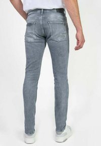 Jeans en denim gris slim fit avec une finition délavée, dotés de deux poches arrière et d'un design minimaliste. Portés avec des baskets blanches.