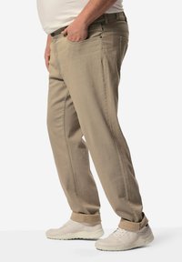 Beige puuvillapantsit rentona leikkauksena, joissa on nappi- ja vetoketjusuljenta, sivutaskut ja käännettävät lahkeet. Yhdistetty valkoisiin tennareihin.